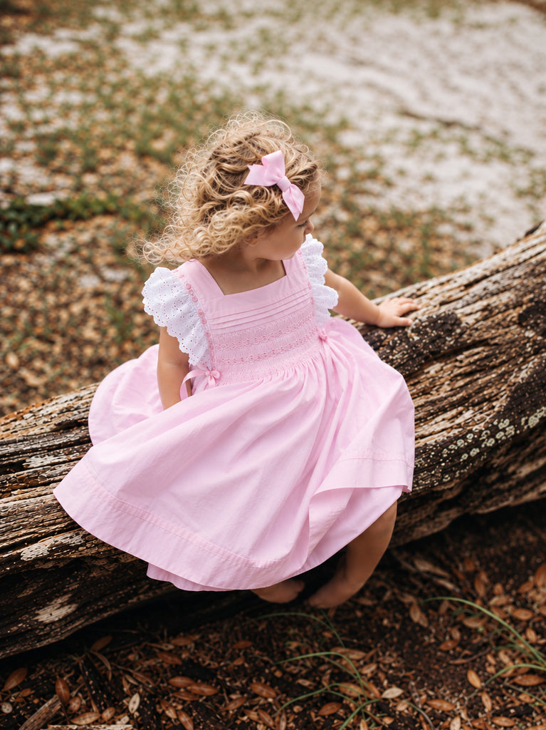 Girl wearing pink hand-smocked dress with white eyelet lace sleeves