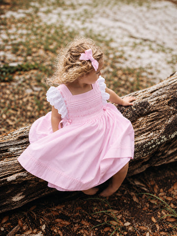 Girl wearing pink hand-smocked dress with white eyelet lace sleeves